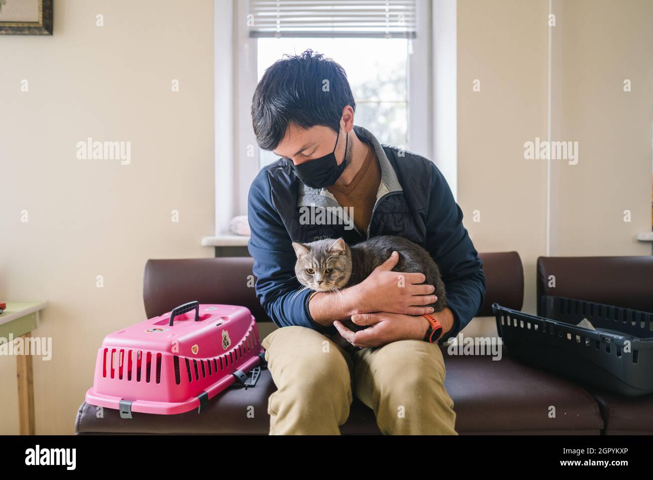 Homme portant un masque de protection avec un animal de compagnie attendant dans le hall pour un examen médical à la clinique vétérinaire. Santé animale. Propriétaire du chat britannique gris qui m'attend Banque D'Images