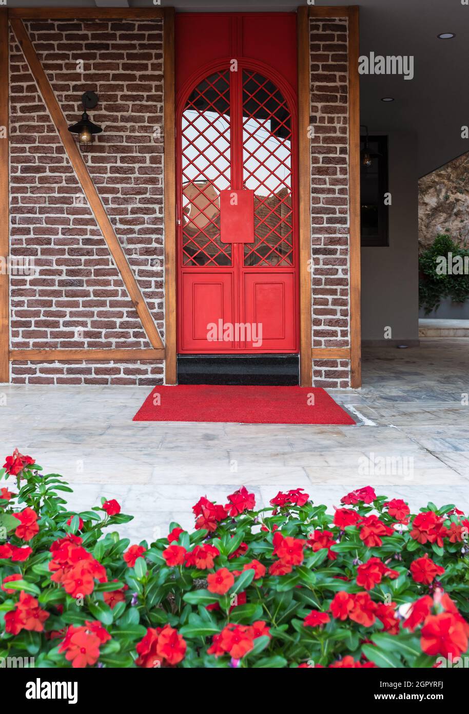 Portes en fer rouge vif entourées de fleurs rouges sur un mur de briques dans une maison turque Banque D'Images