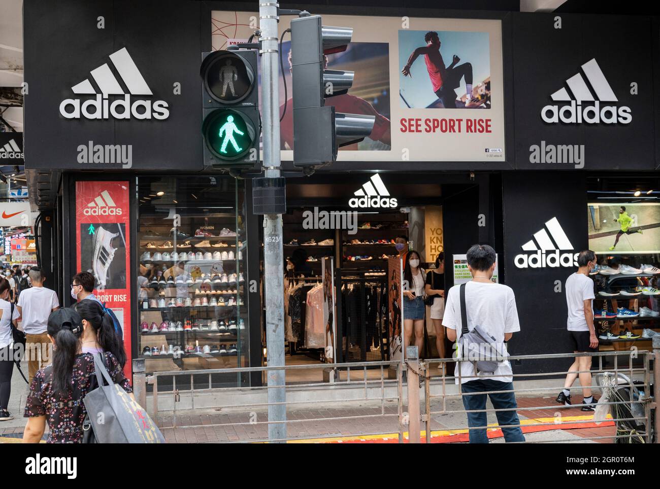 Des piétons marchent devant la marque allemande multinationale de vêtements de sport Adidas magasin et logo à Hong Kong. Banque D'Images