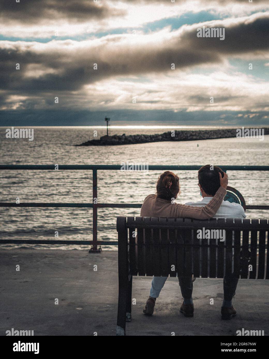 Couple adulte assis sur un banc et regardant la mer sous un ciel nuageux Banque D'Images
