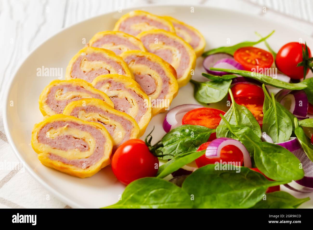 petits-déjeuners au jambon et au fromage hachés avec omelettes et salade d'oignons rouges aux épinards frais sur une assiette sur une table en bois blanc, vue horizontale depuis un Banque D'Images