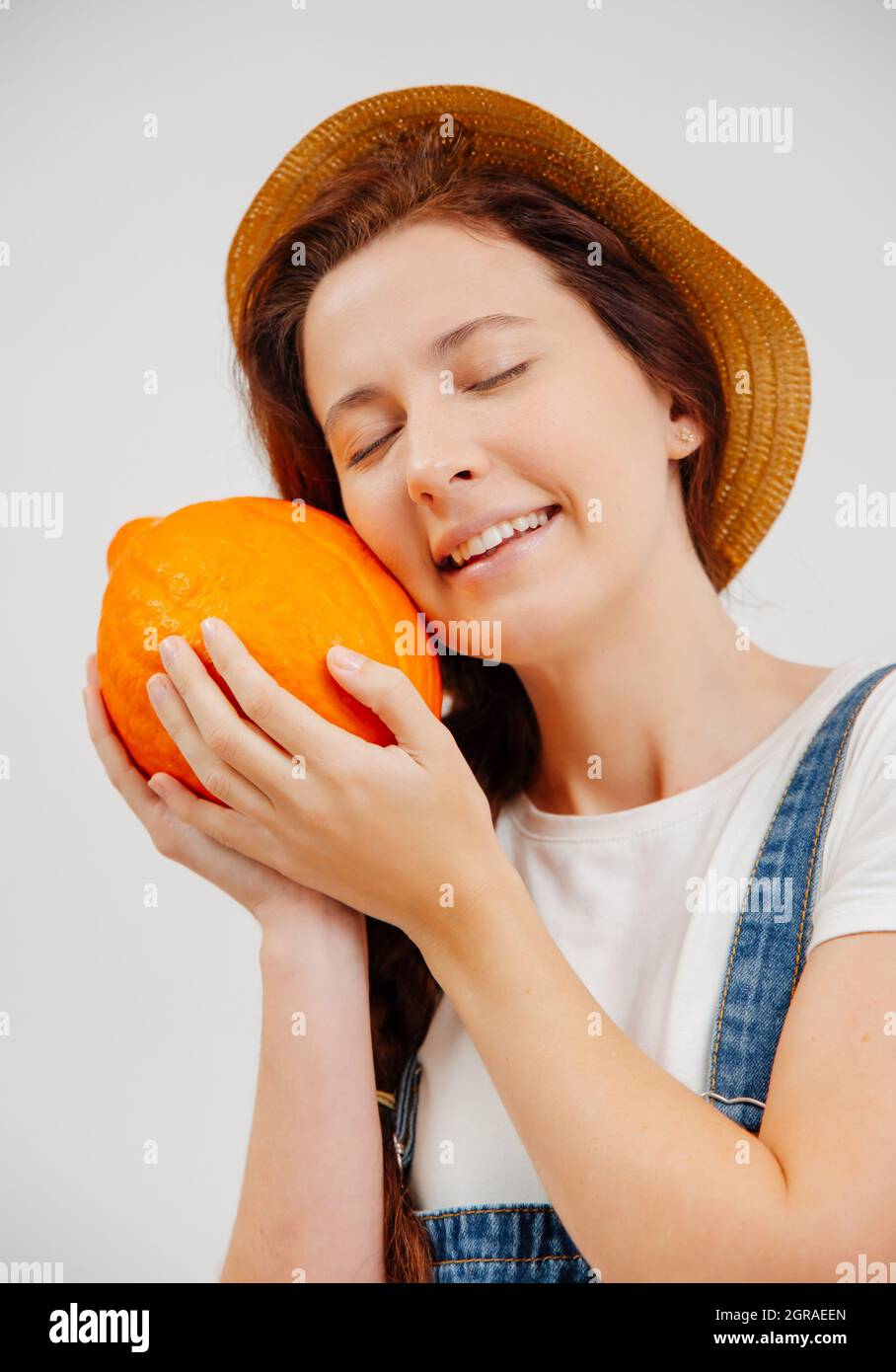 Une femme heureuse en combinaison et un chapeau s'occupe d'une petite citrouille mûre. Banque D'Images