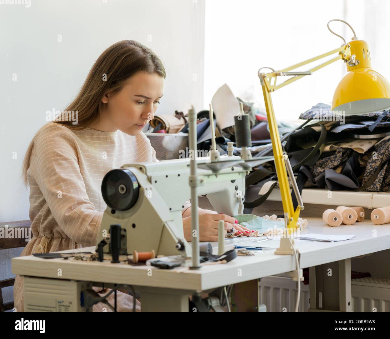 Jeune femme concentrée couturière couture vêtements avec machine à coudre  pendant le travail dans atelier de mode Photo Stock - Alamy