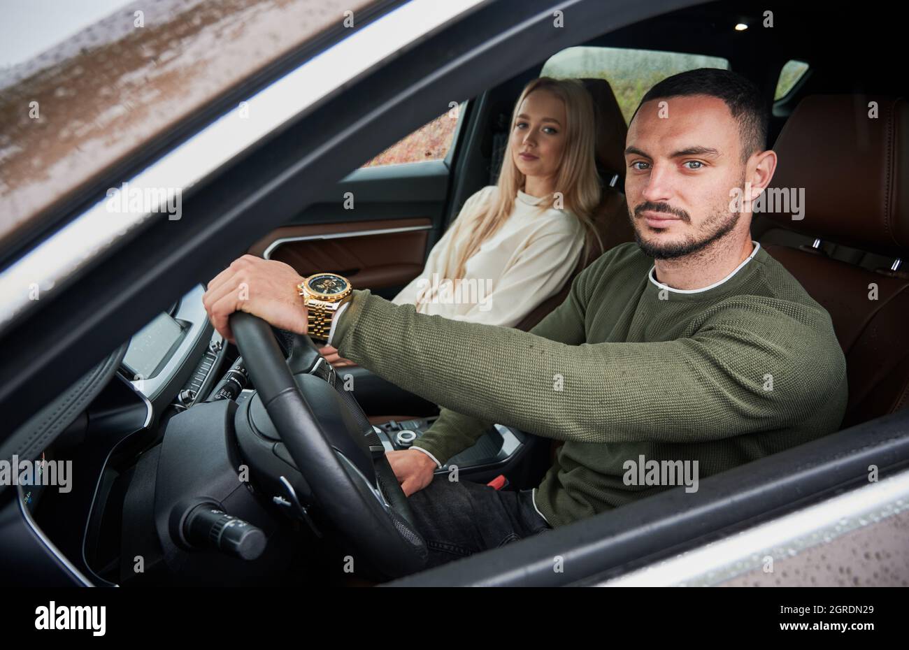 Portrait d'un conducteur homme sérieux et d'une belle femme passager sur le siège avant de la voiture. Jeune conducteur mettant sa main sur le volant, regardant dans la caméra par la vitre latérale abaissée. Banque D'Images