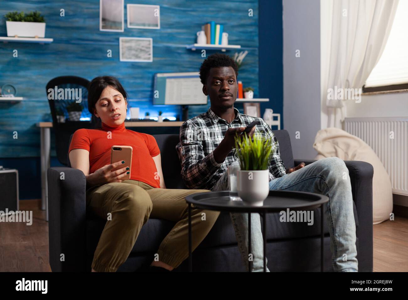 Couple Interracial Avec Grossesse En Attendant Bebe A La Maison Femme Enceinte De Race Blanche Tenant Un Smartphone Alors Qu Un Homme Afro Americain Regarde Un Film A La Television Avec Une Telecommande Photo