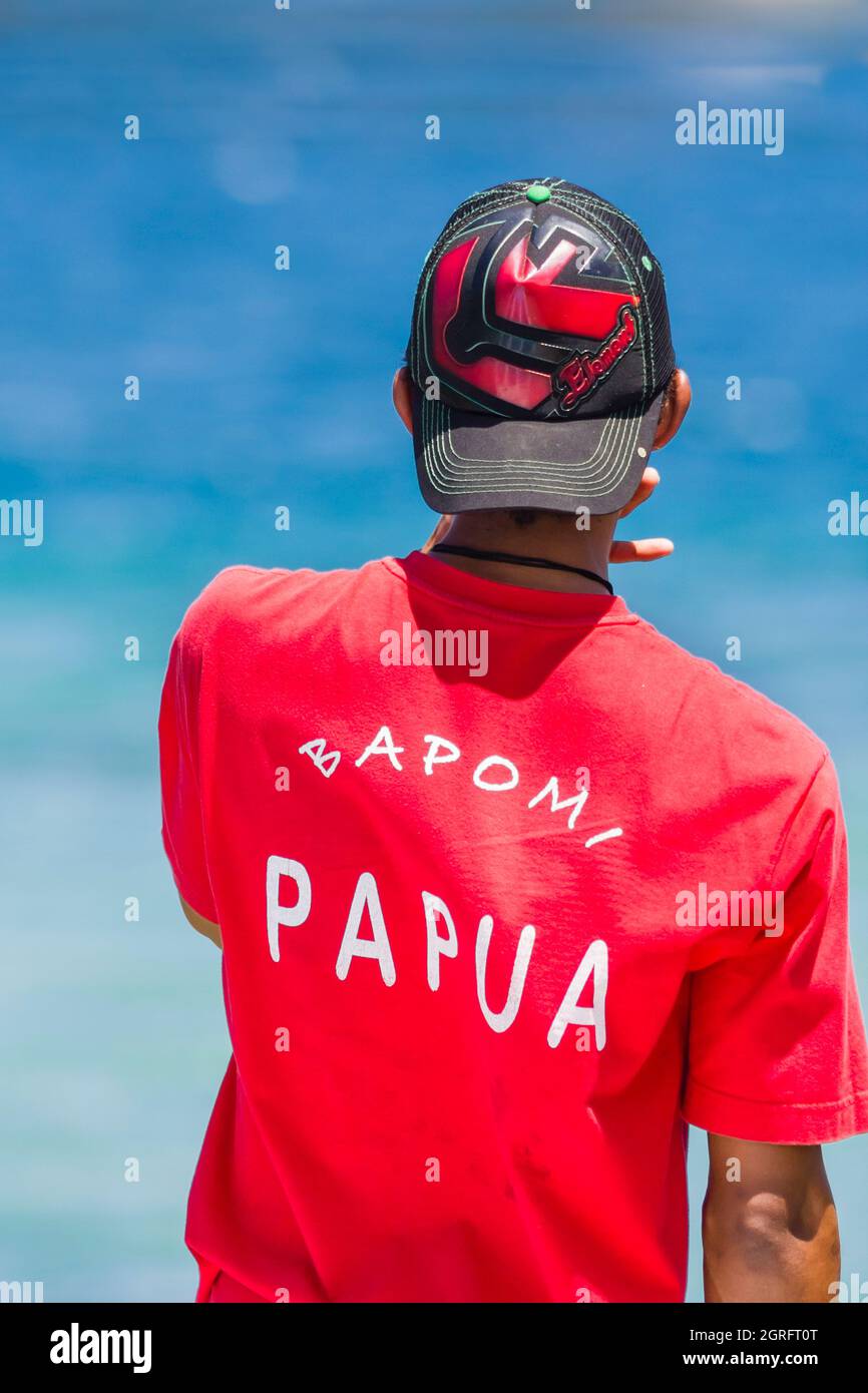 Indonésie, Papouasie, île de Biak, un jeune homme vu de derrière, siffle pour appeler des amis sur un bateau amarré au loin Banque D'Images