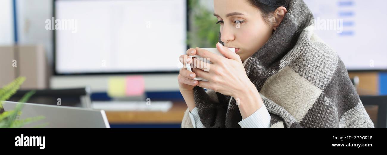 La jeune femme malade est assise dans une couverture chaude avec une tasse sur le lieu de travail Banque D'Images