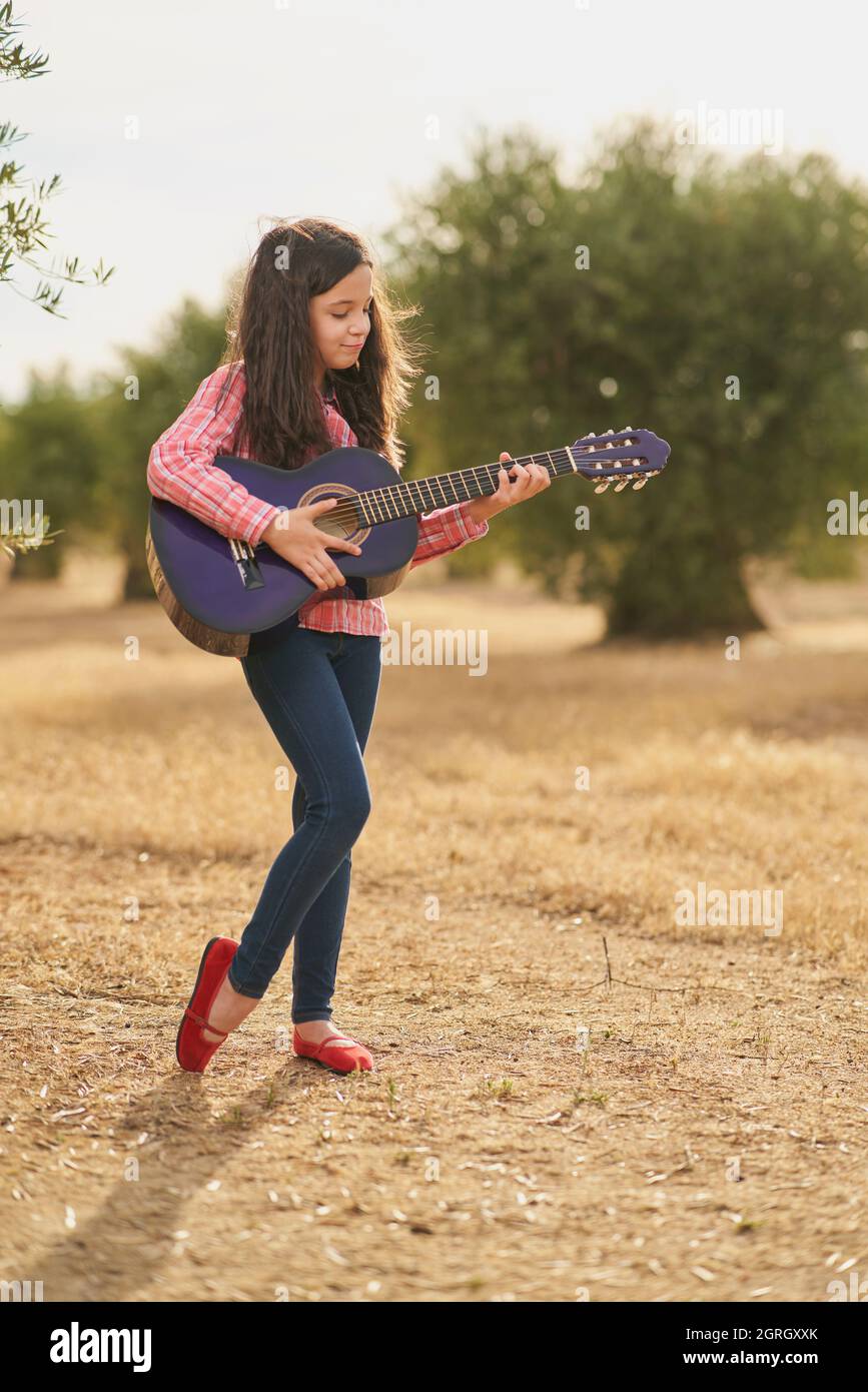 Brunette fille joyeuse jouant sa guitare dans une oliveraie au coucher du soleil Banque D'Images