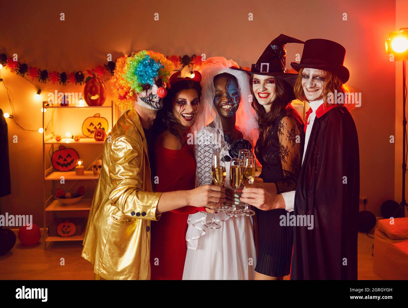 Groupe diversifié de jeunes hommes et femmes heureux de clinking lunettes lors d'une fête d'Halloween Banque D'Images