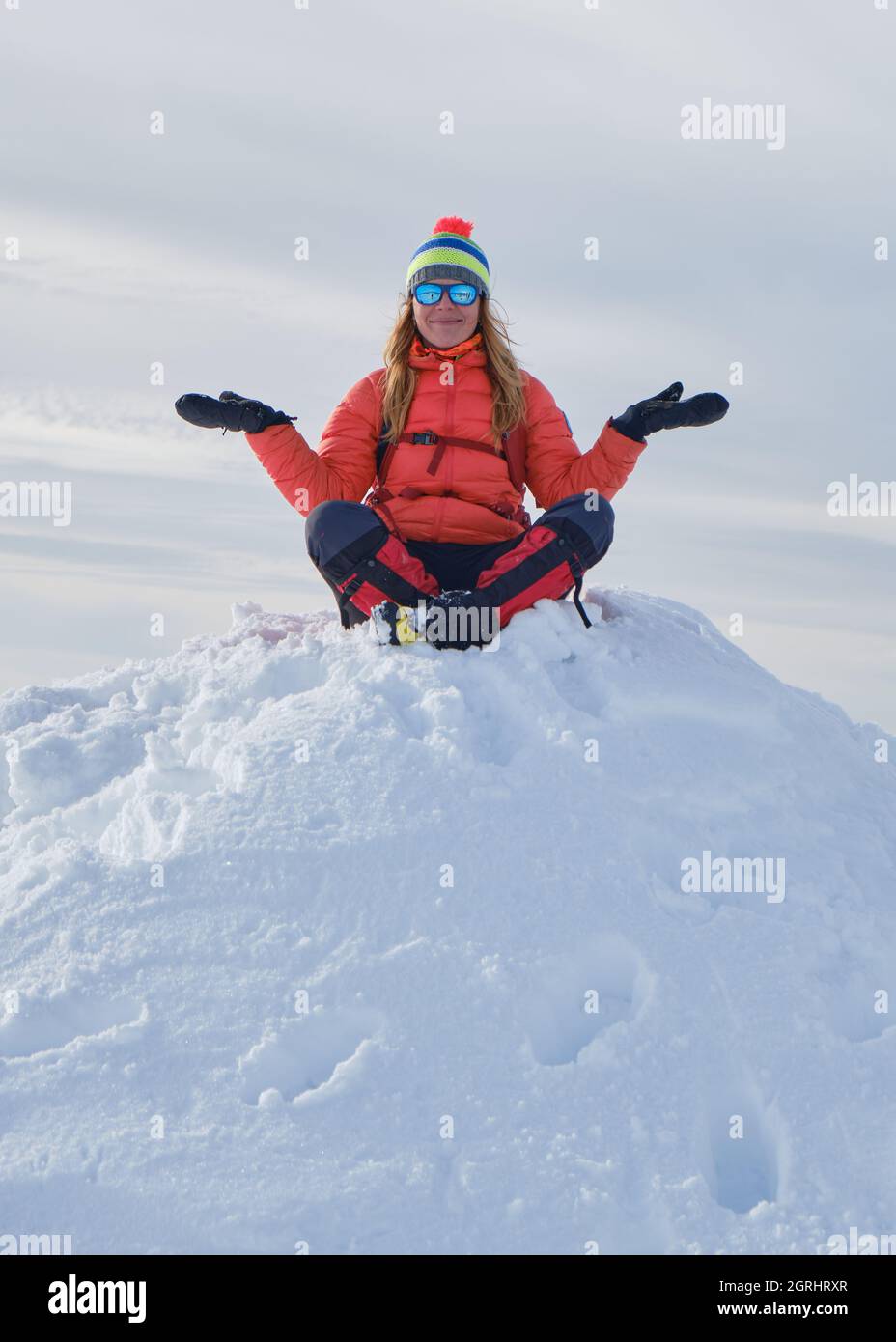 Femme randonneur portant des vêtements chauds d'hiver se trouve sur la pile de neige avec ses bras étirés et ses jambes croisées, heureux et souriant. Sommet, haut, goa Banque D'Images