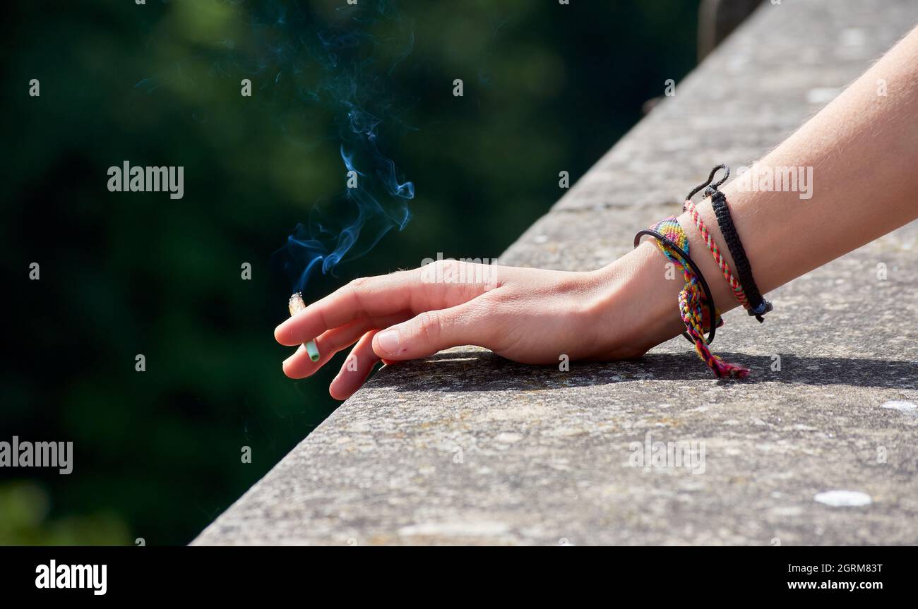 Main de femme portant des bracelets penchée sur une structure en pierre tenant une cigarette allumée Banque D'Images