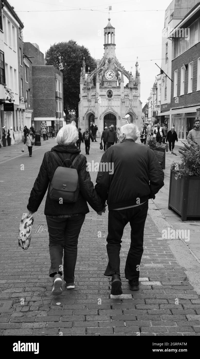 Un couple de personnes âgées à pied main dans la main dans le centre-ville de Chichester Banque D'Images