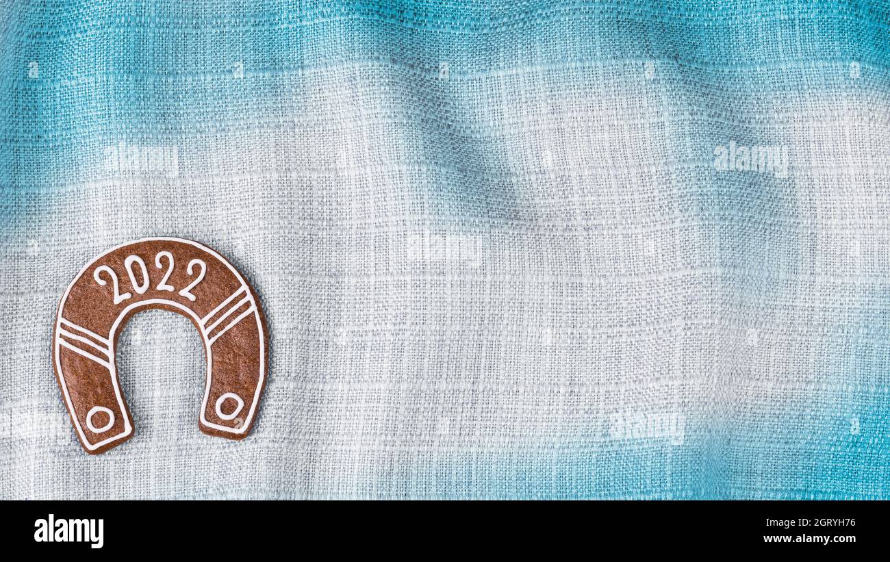 Fer à cheval du nouvel an très orné pour la chance en 2022 sur fond de tissu ondulé blanc bleu. Magnifique biscuit en forme de chaussure de cheval sur la texture de toile froissée. Banque D'Images