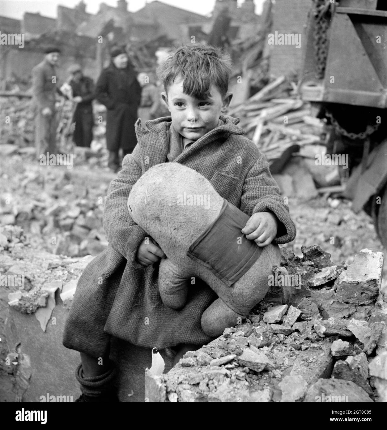 Un garçon malheureux et choqué tenant un animal en peluche dans les ruines après le bombardement aérien allemand de Londres, Angleterre. Banque D'Images