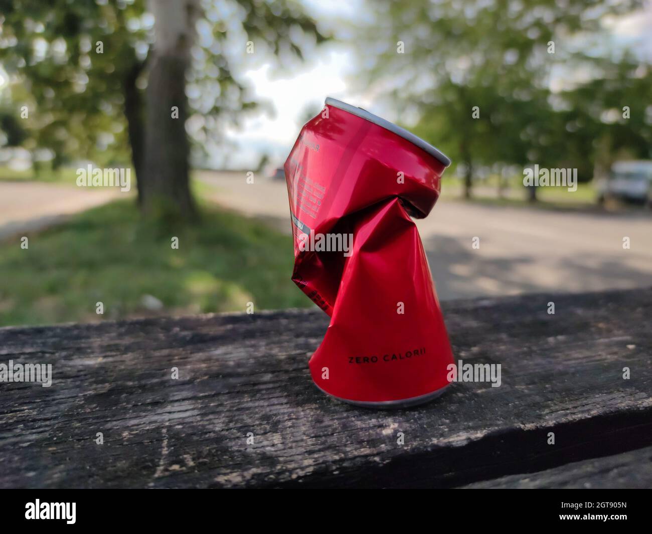 Canette de soda émietlée avec l'inscription « zéro calories » (roumain : zéro calori) sur un banc dans un parking en bord de route. Banque D'Images