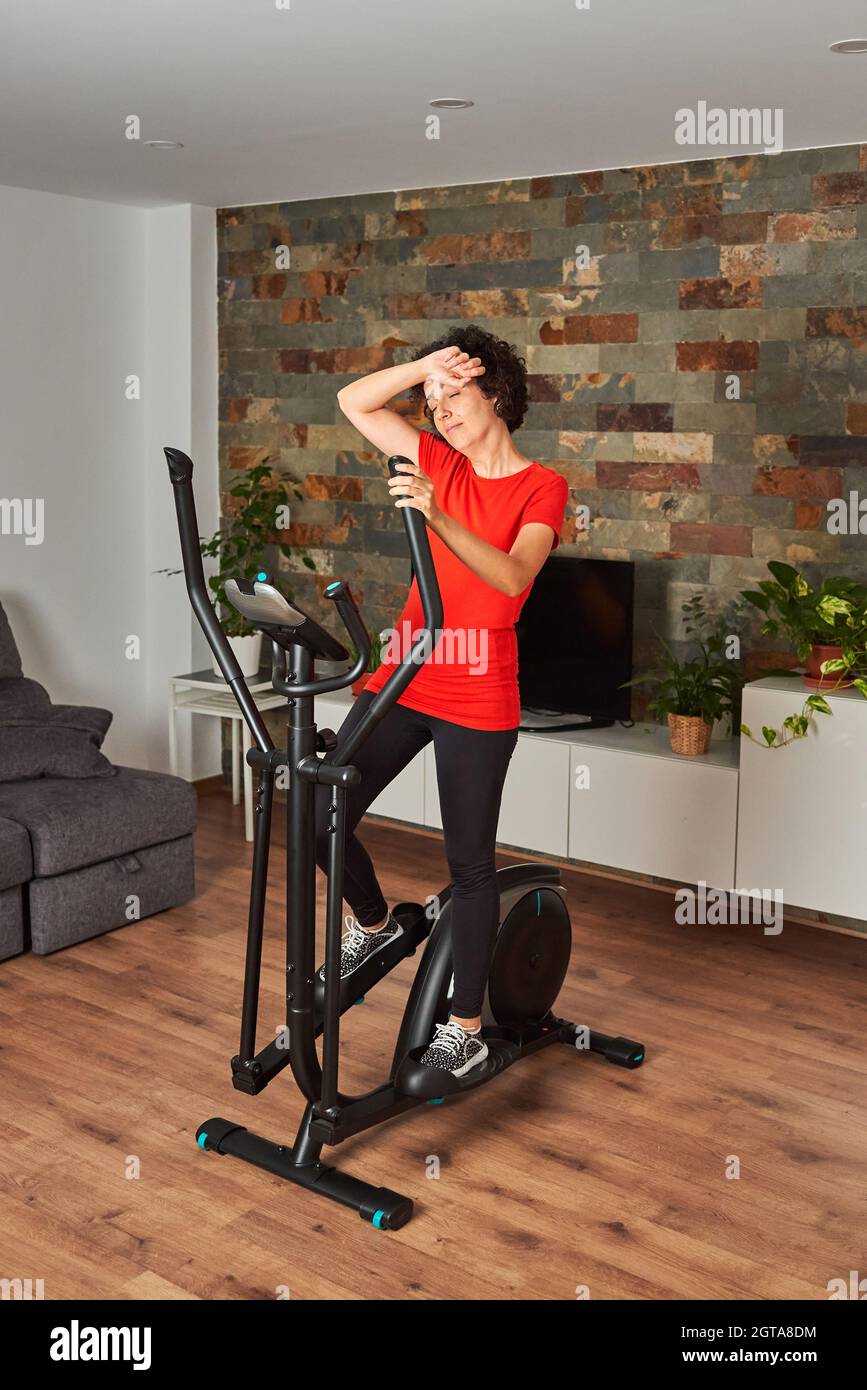 Une femme s'entraîne à la maison en utilisant un vélo elliptique Banque D'Images
