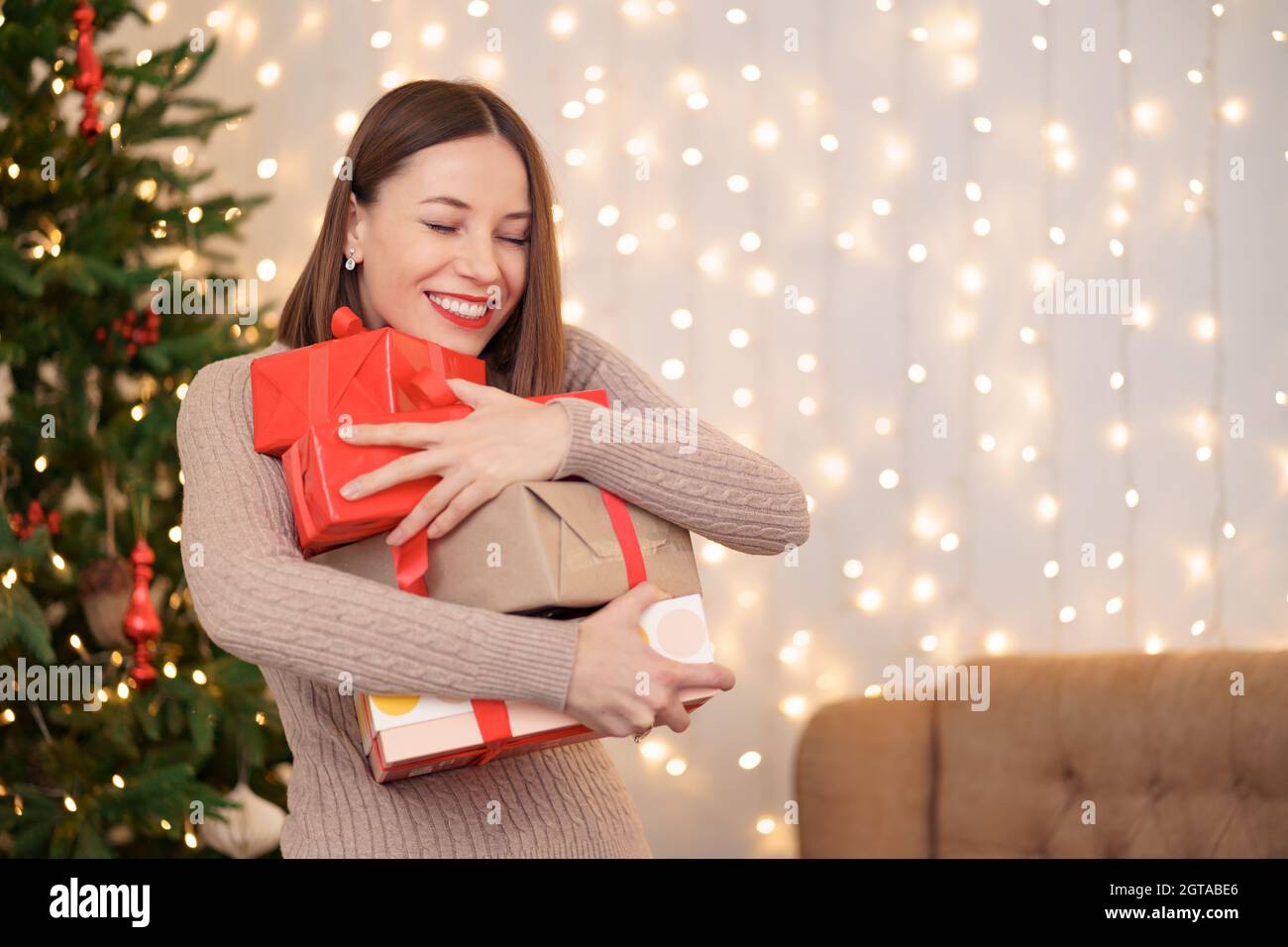 Bonne jeune femme tenant beaucoup de boîtes présentes avec arbre de Noël et s'allume en arrière-plan Banque D'Images