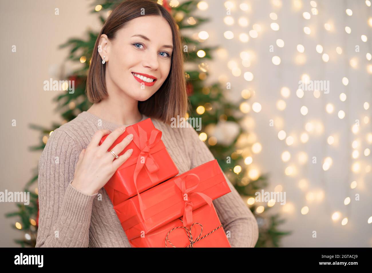Bonne jeune femme tenant beaucoup de boîtes présentes avec arbre de Noël et s'allume en arrière-plan Banque D'Images