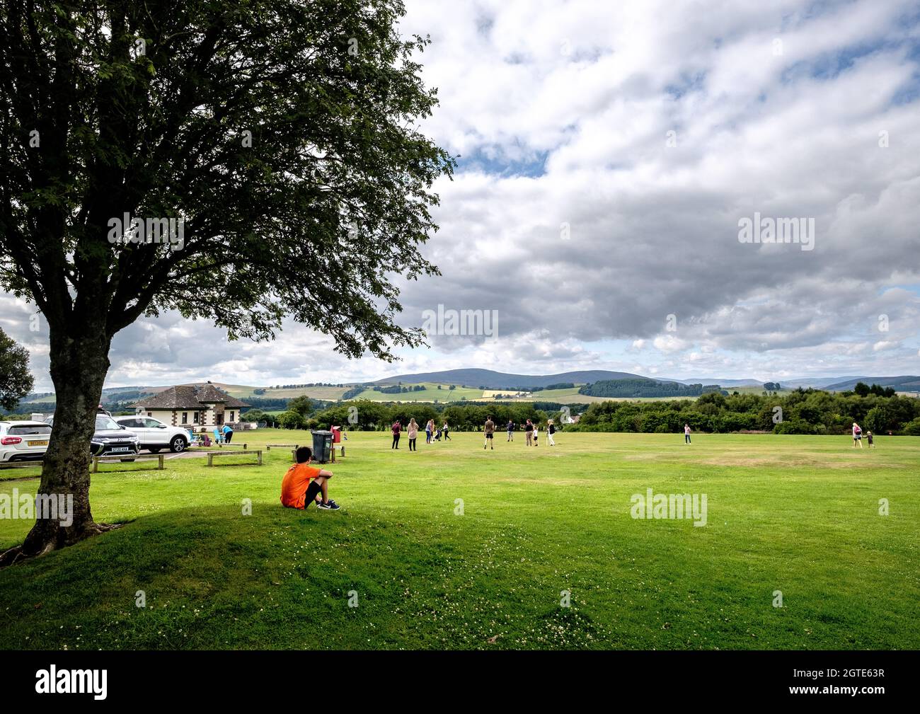 Un garçon sous un arbre observe une famille et des amis qui jouent au cricket à l'extérieur du bâtiment de Camera Obscura, sur la colline de Kirriemuir, Angus, en Écosse Banque D'Images
