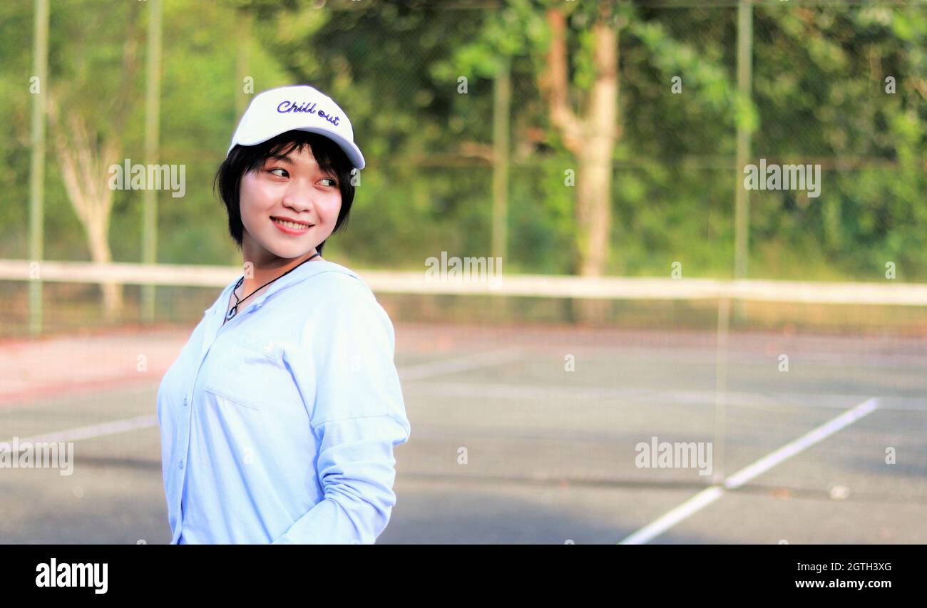 Belle femme asiatique aux cheveux courts, portant un chapeau et souriant  largement sur le court de tennis Photo Stock - Alamy
