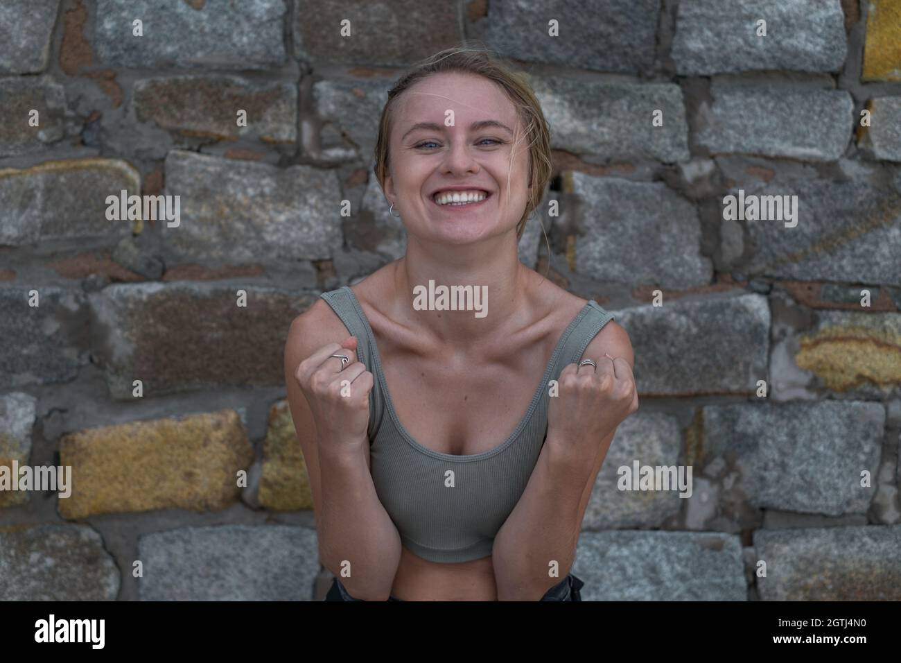 Portrait d'une jeune femme blonde de race blanche heureuse et satisfaite en haut de la récolte sur fond de pierre. Concept des émotions humaines, expression faciale. Amusé Banque D'Images