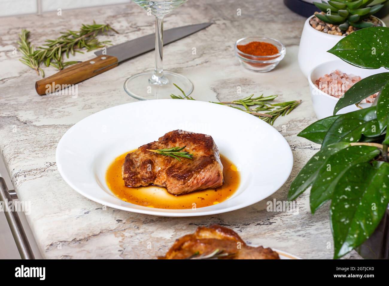 Steak de bœuf rôti fraîchement préparé avec épices et romarin sur une assiette ronde blanche sur le fond de la table de cuisine. Banque D'Images