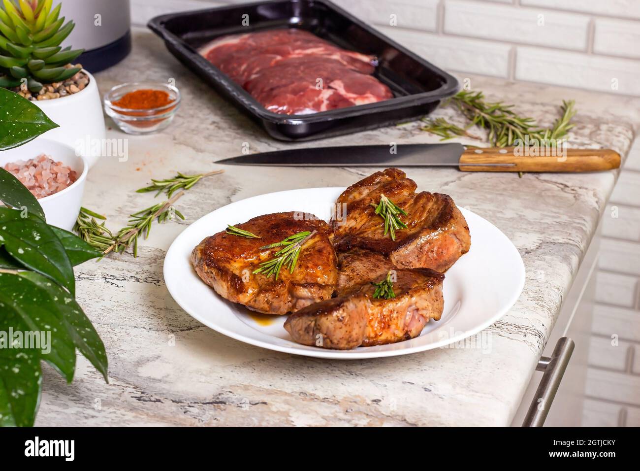 Steak de bœuf rôti fraîchement préparé avec épices et romarin sur une assiette ronde blanche sur le fond de la table de cuisine. Banque D'Images