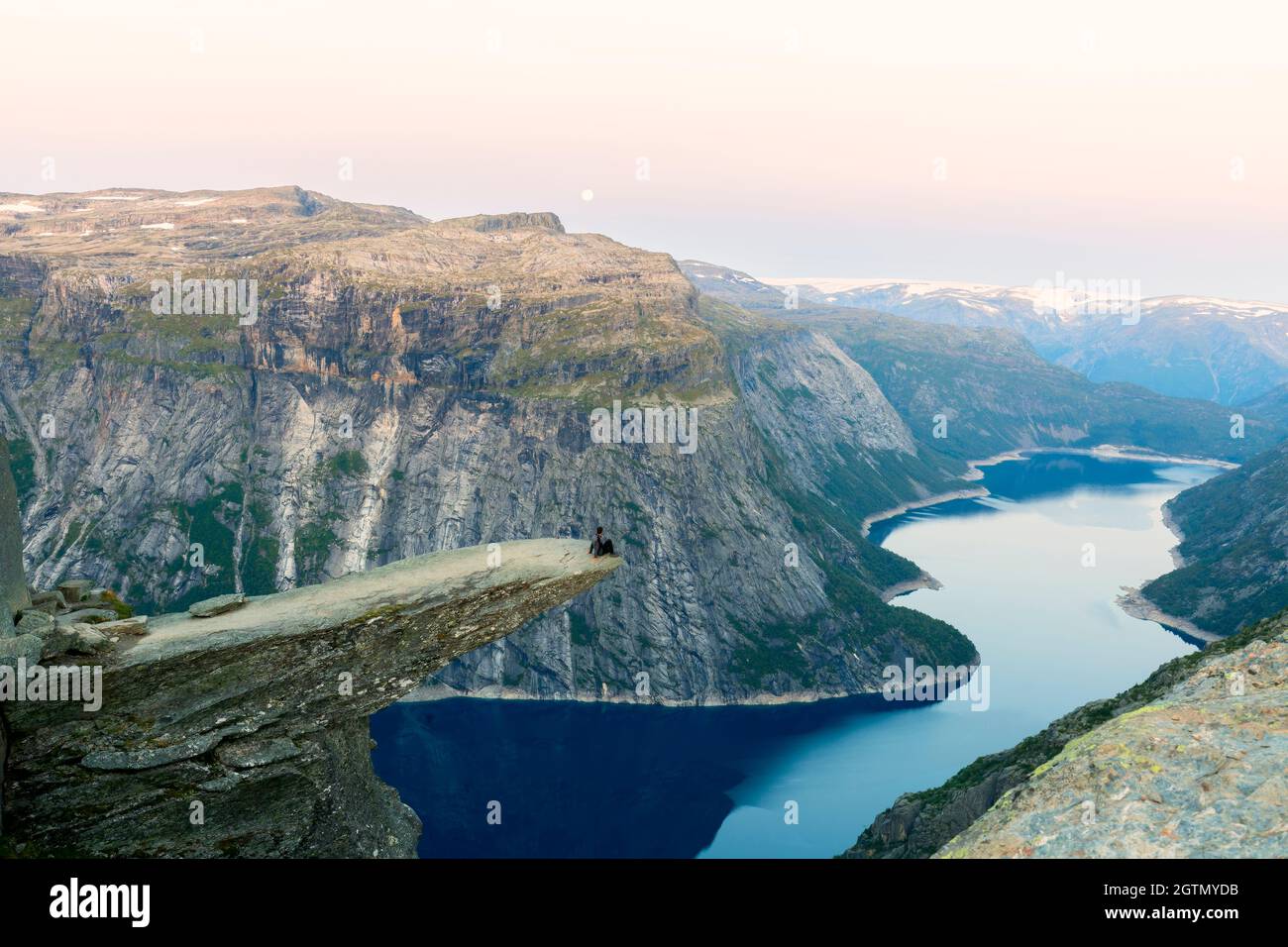 Superbe vue sur la nature avec Trolltunga et un homme assis dessus au coucher du soleil sous la lune. Emplacement: Montagnes scandinaves, Norvège, Odda. Image artistique. Banque D'Images