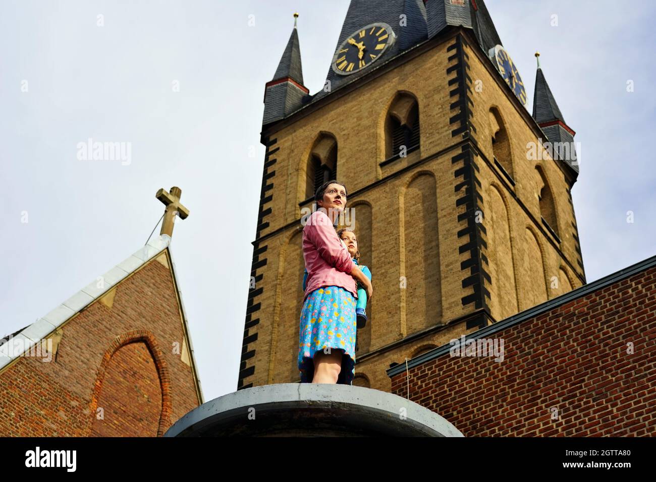 Sculpture réaliste 'Säulenheilige' d'une mère avec son enfant par l'artiste Christoph Pöggeler. Église Saint-Lambertus en arrière-plan. Banque D'Images