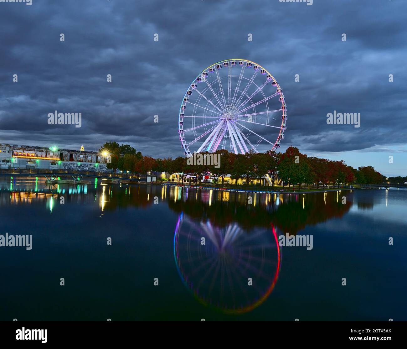 Longue exposition de la grande roue de Montréal dans le Vieux-Port à l'heure bleue du crépuscule. L'arrière-plan est ciel nuageux et nuageux. Le premier plan correspond aux arbres de couleur d'automne et Banque D'Images