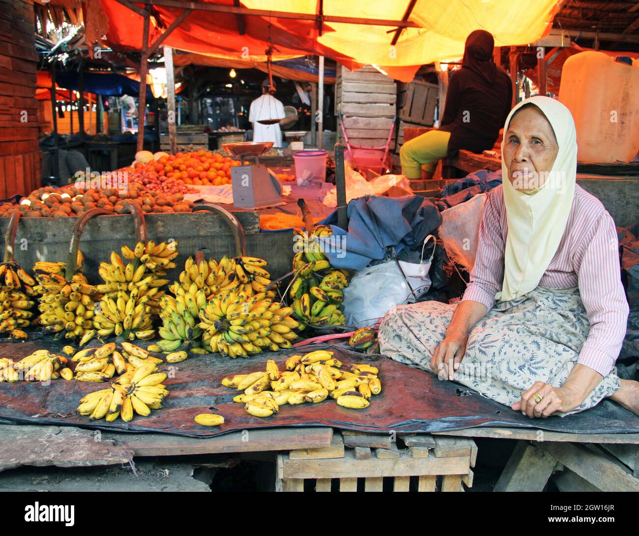 Une vieille femme qui vend des bananes dans un marché en décrochage à Padang, dans l'ouest de Sumatra, en Indonésie.Elle est assise à pattes croisées et porte un hijab musulman, Banque D'Images