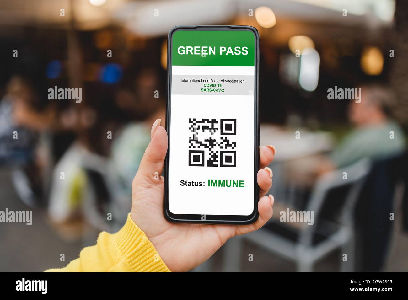 Certificat de passe vert numérique immunitaire pour le vaccin coronavirus avec bar restaurant sur fond - Focus sur la main de femme tenant le téléphone mobile Banque D'Images