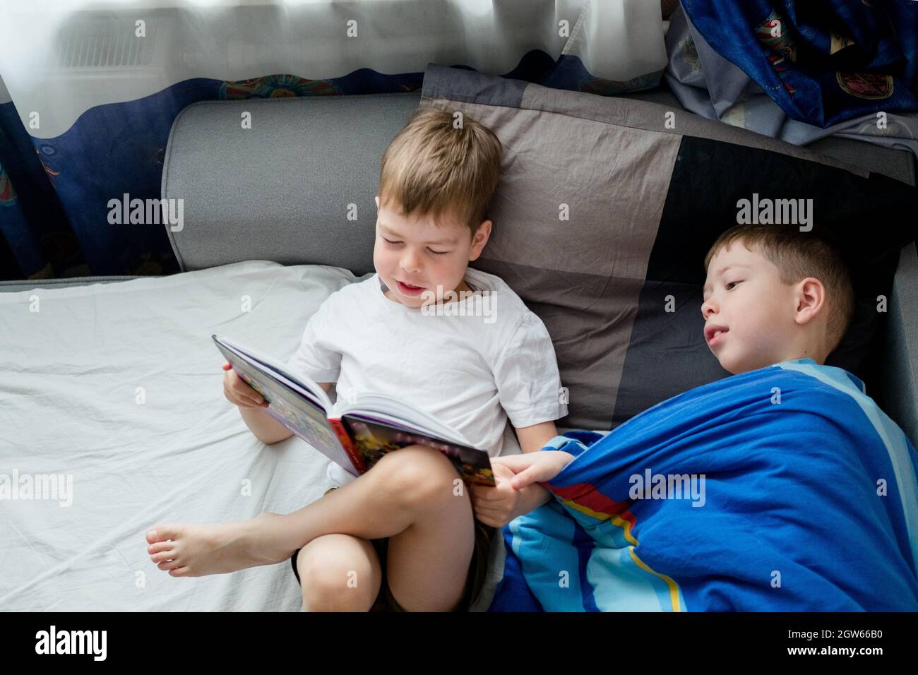 un petit frère lit un livre sur le lit pour un aîné.Amitié entre frères.Amour pour la lecture.Lark et hibou parmi les gens.2 garçons sur le lit Banque D'Images