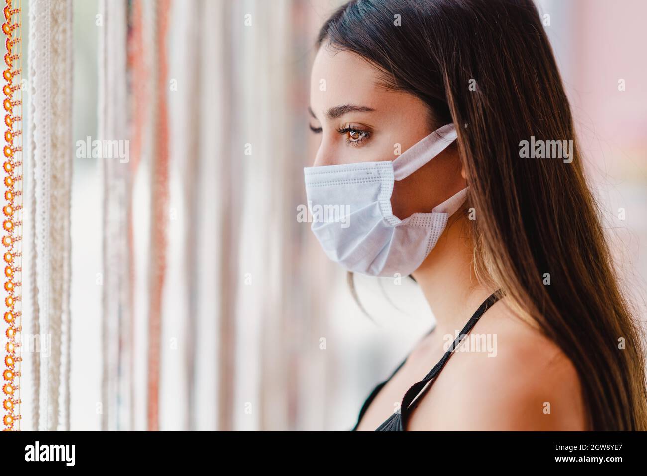 La jeune femme est debout et regarde de la fenêtre avec un masque de protection sur son visage. La rupture du virus Corona. Photo de haute qualité Banque D'Images