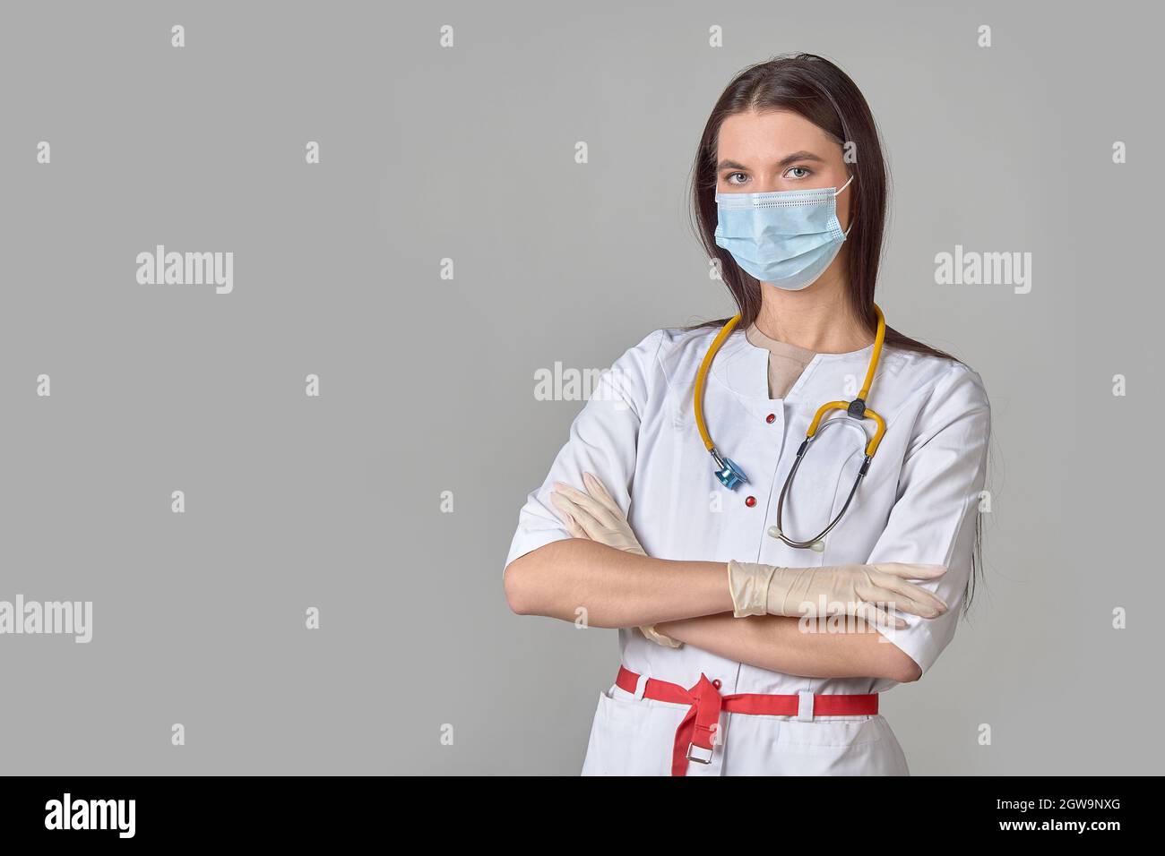 Une jeune femme médecin en manteau blanc avec un stéthoscope et un masque médical sur fond gris isolé Banque D'Images