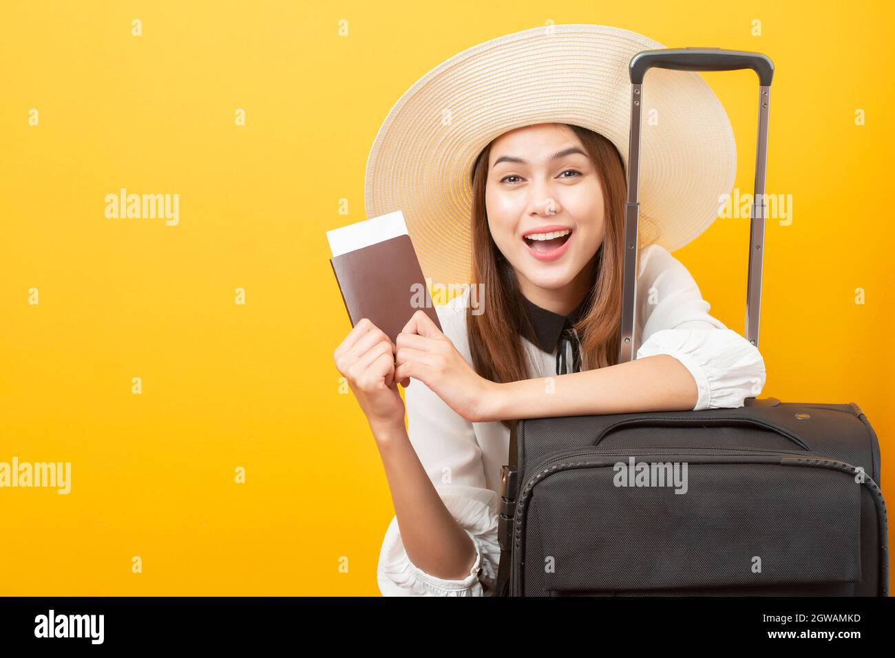 Portrait d'une jeune femme souriante tenant un passeport tout en étant assise avec Suitcase contre fond jaune Banque D'Images