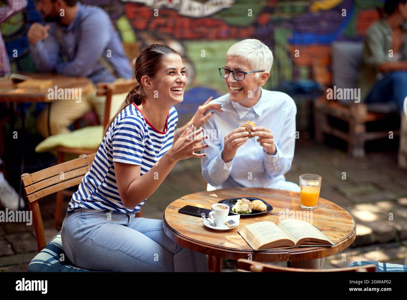 les femmes âgées et les jeunes adultes rient au café en plein air, prenant le petit déjeuner et un merveilleux moment. différent âge femmes amis concept de relation. Banque D'Images
