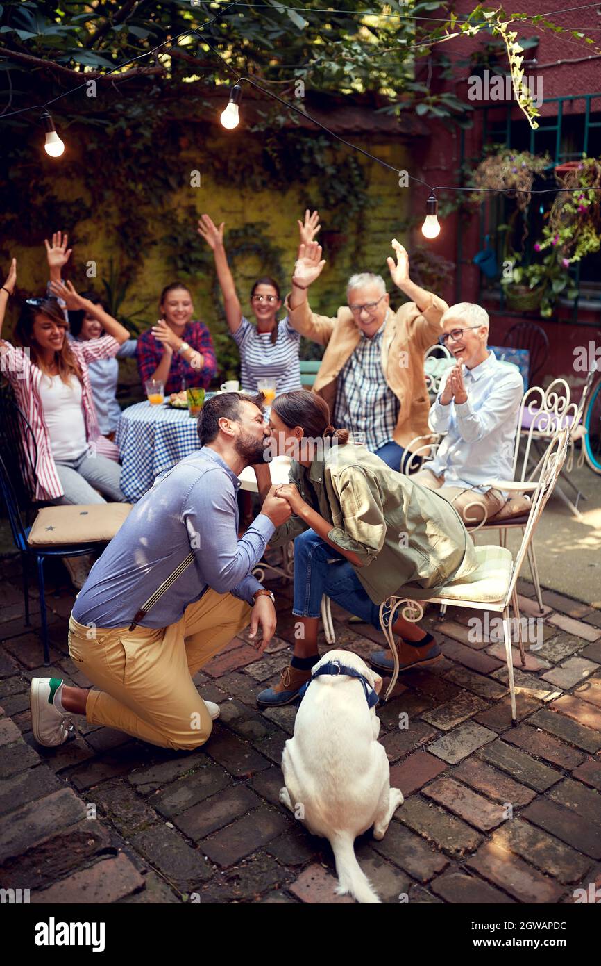 un moment merveilleux sur l'appareil photo. Juste proposé femelle embrassant son homme, devant les membres de la famille et les amis les plus proches et un chien. PET est un membre de famille Banque D'Images un moment merveilleux sur l'appareil photo. Juste proposé femelle embrassant son homme, devant les membres de la famille et les amis les plus proches et un chien. PET est un membre de famille Banque D'Images