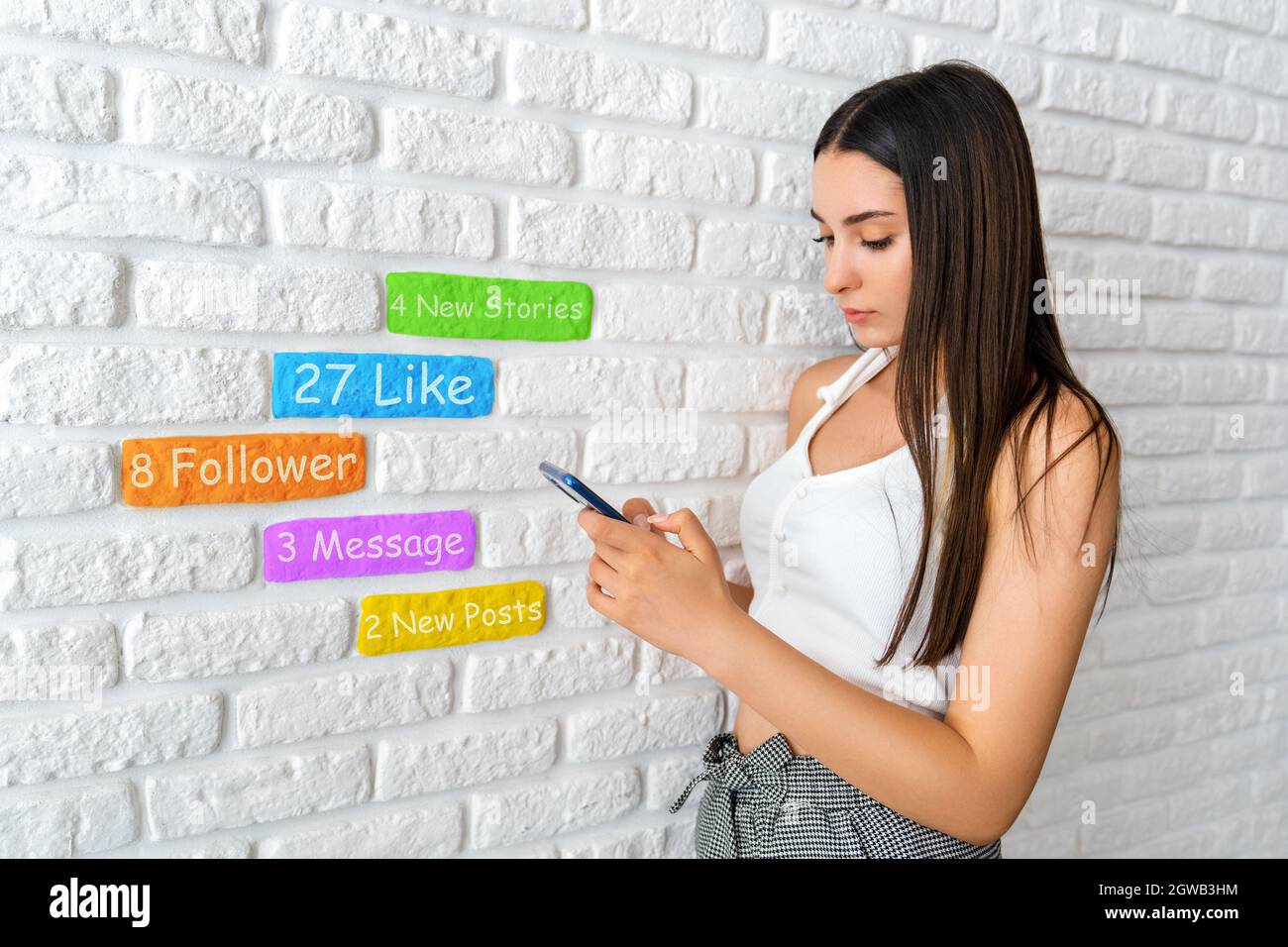 Une jeune femme est debout devant un mur de briques blanches et vérifie les médias sociaux avec son smartphone. Photo de haute qualité Banque D'Images