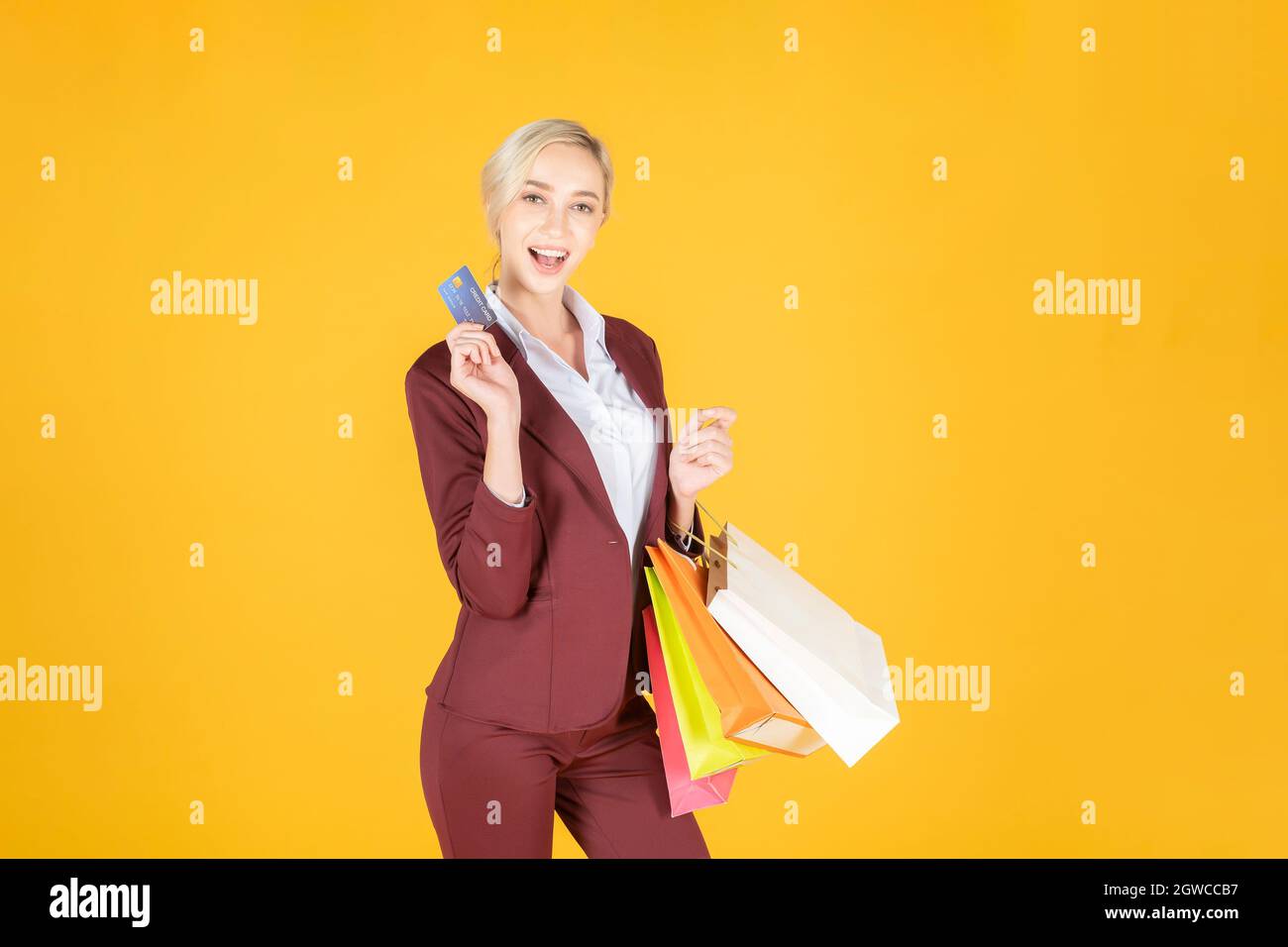 Portrait d'une jeune femme tenant des sacs de shopping et une carte de crédit sur fond jaune Banque D'Images