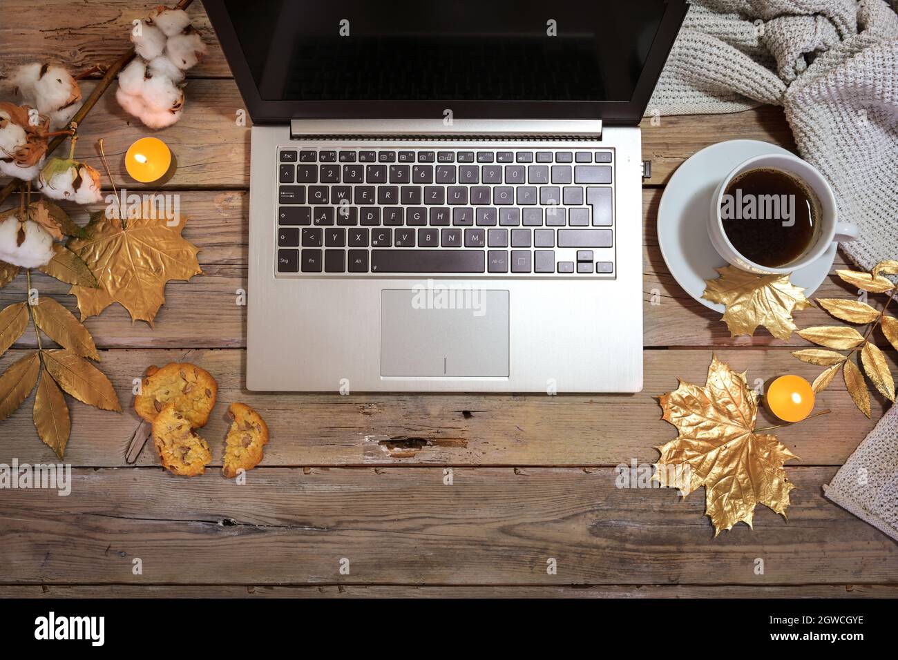 ordinateur portable et une tasse de café sur une table rustique en bois décorée avec des feuilles d'automne peintes en or et des bougies, confortable bureau à la maison, plat par le dessus, Banque D'Images
