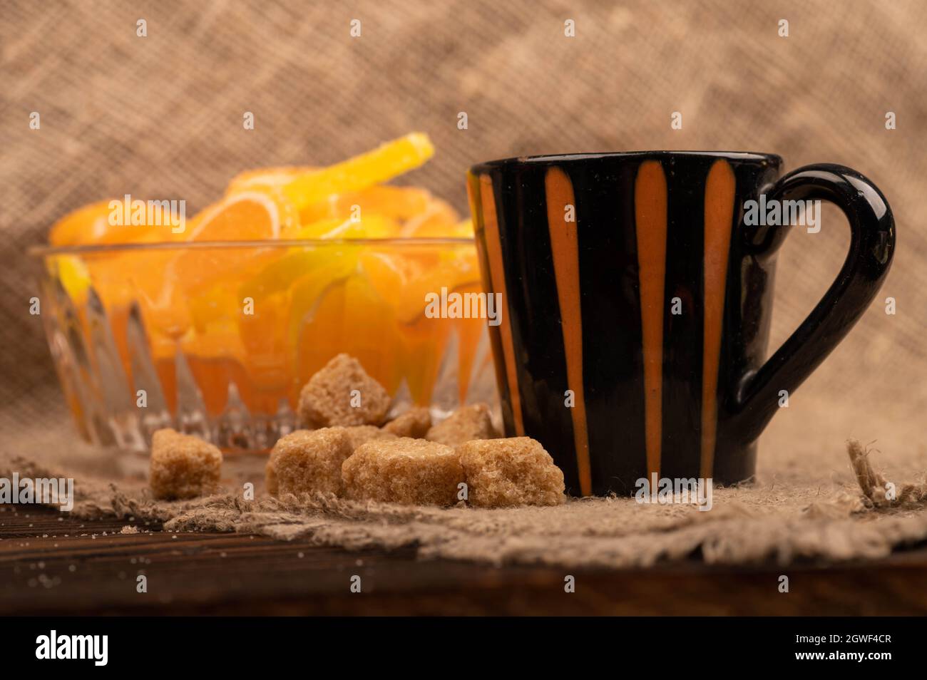 Tranches de citron marmelade multicolores dans un vase en verre, morceaux de sucre de canne brun et une tasse de café, gros plan, mise au point sélective Banque D'Images