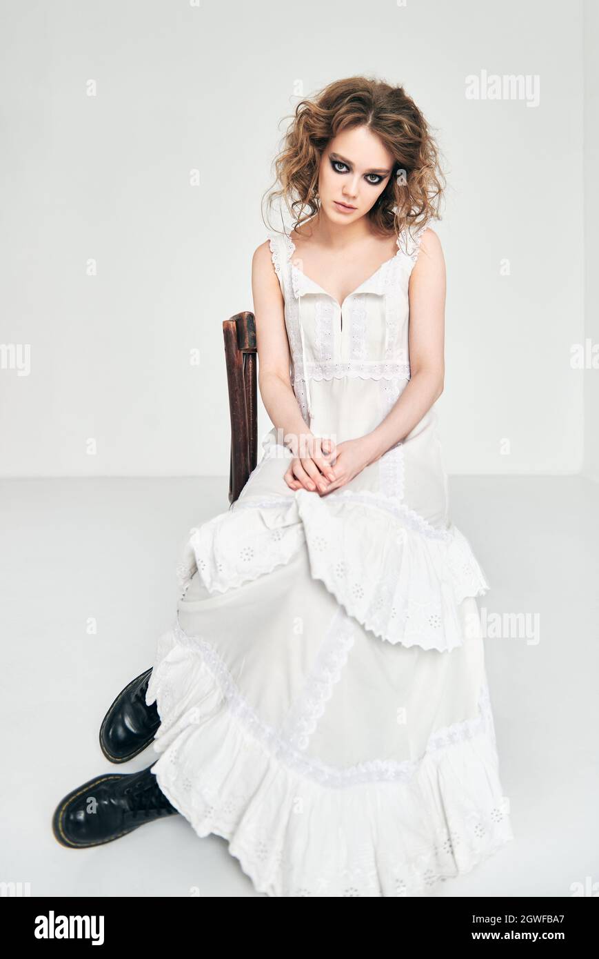 Portrait d'une jolie fille triste étrange. Belle jeune femme impaire en  robe blanche assise sur une chaise dans la chambre vide Photo Stock - Alamy