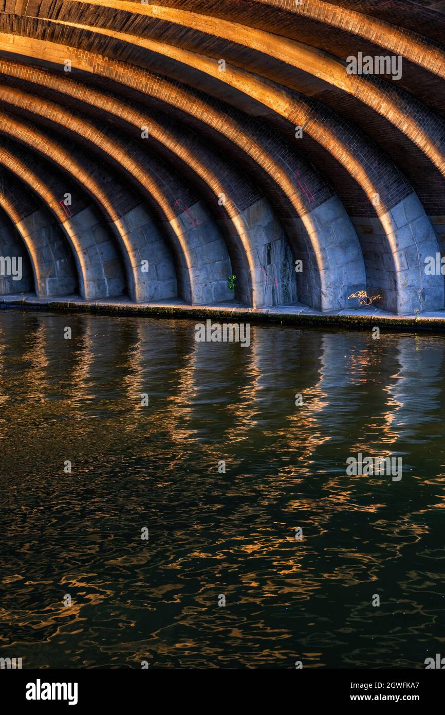Lignes incurvées ensoleillées sous l'ancien pont ferroviaire au coucher du soleil, arc abstrait en brique et structure en pierre avec réflexion dans l'eau, Berlin, Allemagne. Banque D'Images