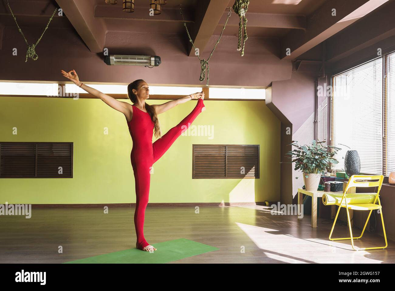 Femme en combinaison rouge pratiquant le yoga tout en se tenant sur un tapis dans le studio faisant l'exercice utthita hasta padangusthasana Banque D'Images