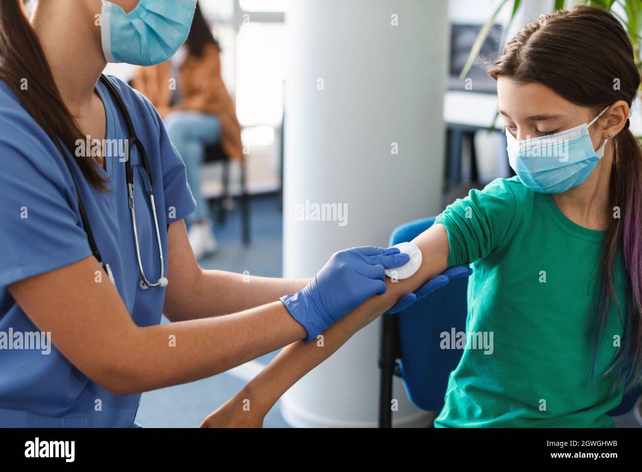 Gros plan de l'infirmière dans le masque facial et les gants désinfection de la peau de l'enfant fille, frottant l'épaule avec le tampon de coton avant l'injection dans le centre de santé, clinique bac Banque D'Images