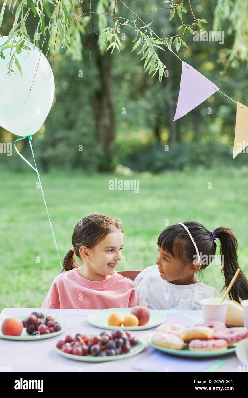 Portrait vertical de deux petites filles à la table de pique-nique en plein air en appréciant la fête d'anniversaire en été Banque D'Images