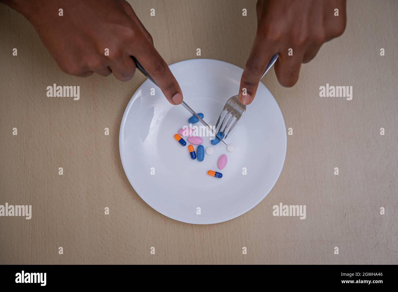 Gros plan des mains coupant des pilules de médicaments psychiatriques avec fourchette et couteau - concept de la santé mentale et des médicaments Banque D'Images