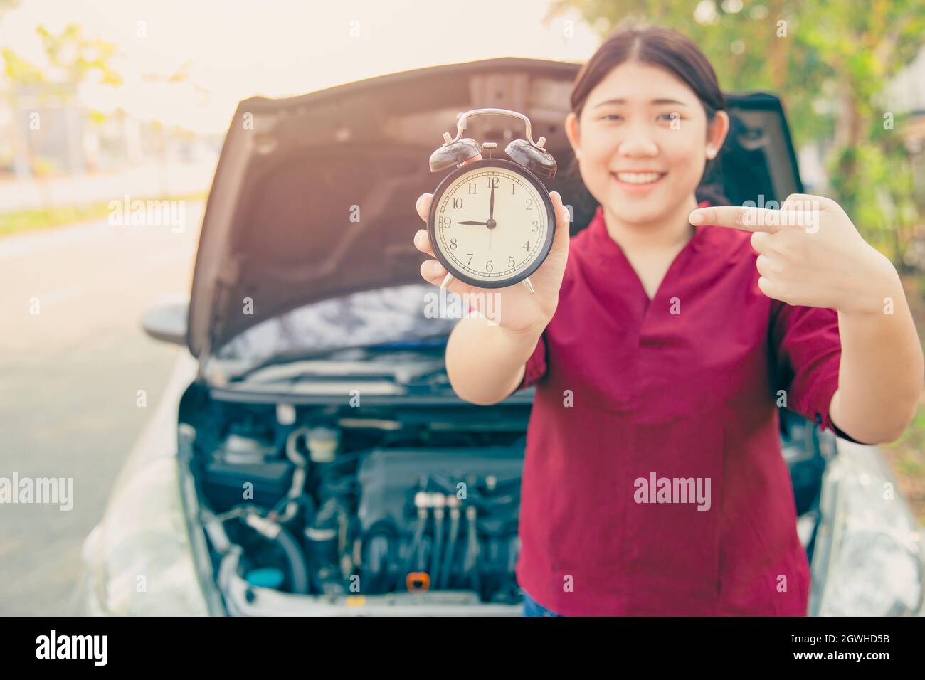 Service de voiture selon les horaires concept, femme sourire heureux avec réveil et arrière-plan de capot ouvert de voiture. Banque D'Images