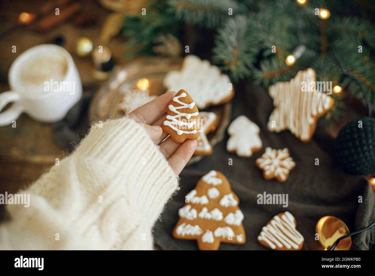 Main tenant l'arbre de noël biscuit de pain d'épice sur fond rustique moody avec des lumières chaudes, café, branches de sapin sur la serviette et table en bois. Hiver à Banque D'Images